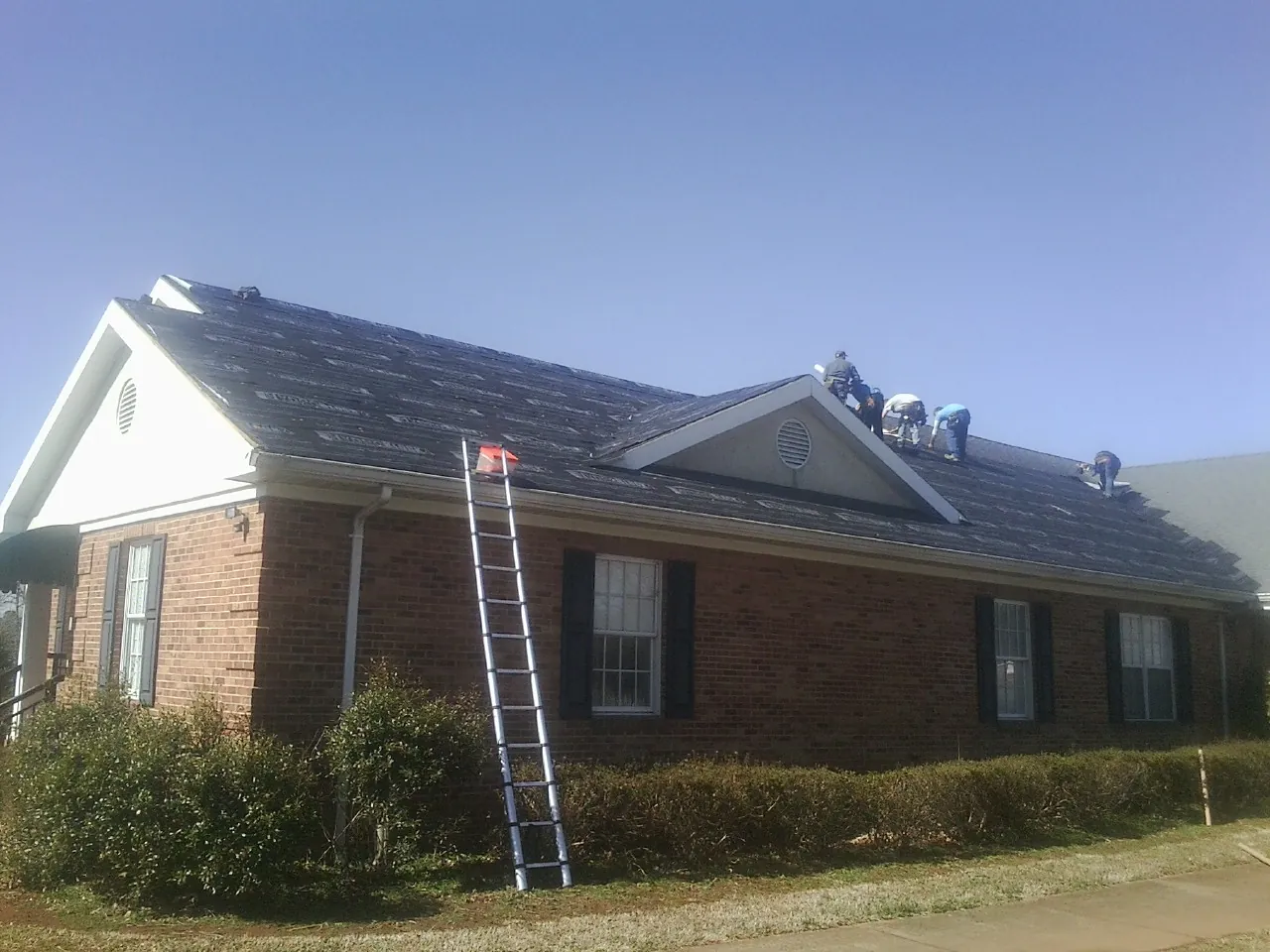 Crew tearing shingles off a brick ranch roof with a ladder set — Metal Roof Repair work by our crew in Greencastle