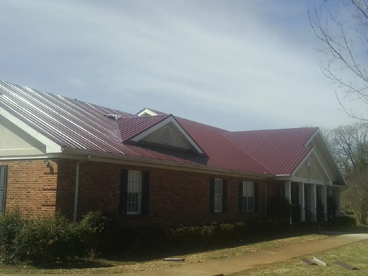 Red metal roof with gabled entries on a long brick building, from a Hail Damage Roof Repair job in Greencastle