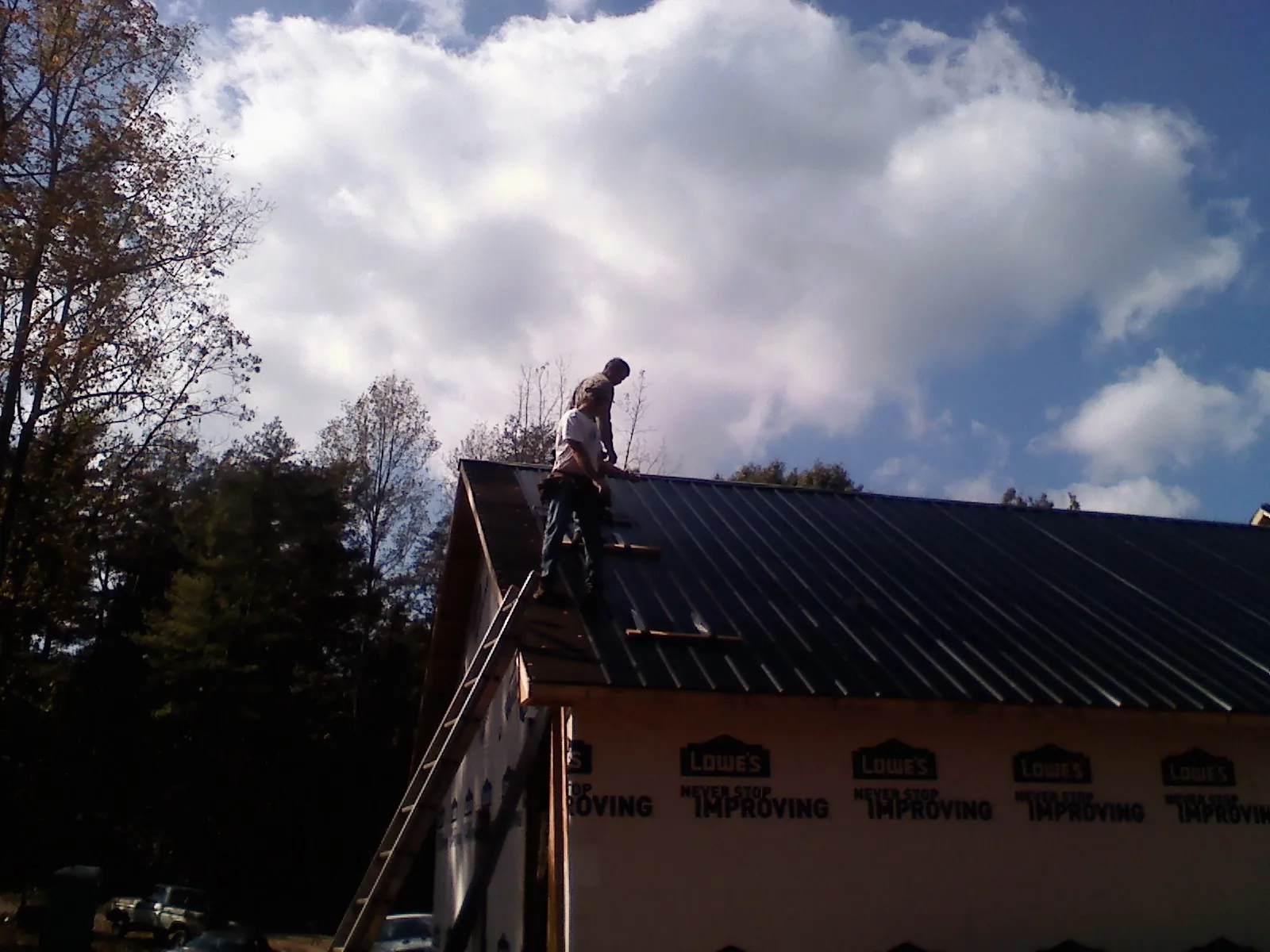 Roofer fastening dark metal panels high against a cloudy sky, from a Roof Inspection job in Greencastle